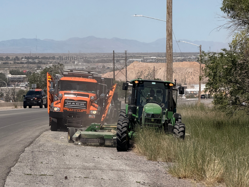 A double-wing plow follows a tractor pulling a mower through tall grass next to a road in Salt Lake City.