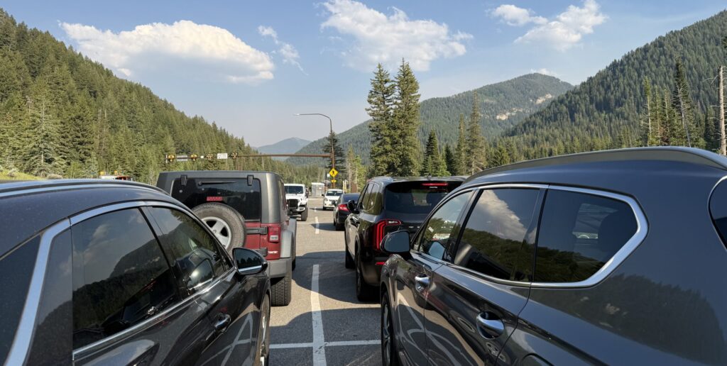 Vehicles parked in the Cardiff Fork / Mill D North & South parking lot in Big Cottonwood Canyon, surrounded by forested mountains under a blue sky.