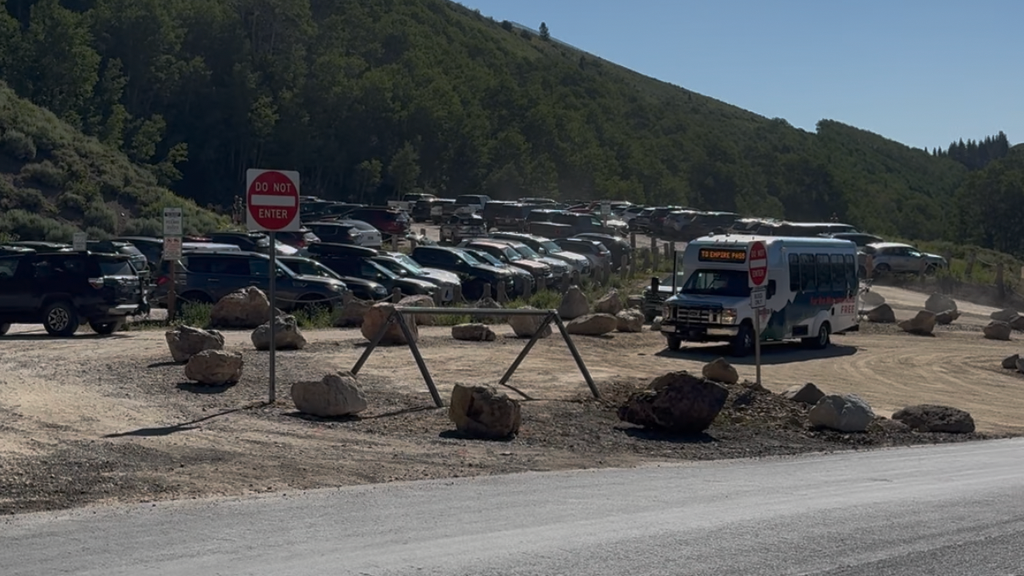 A bus stops at Bloods Lake dirt parking lot that is full of cars.